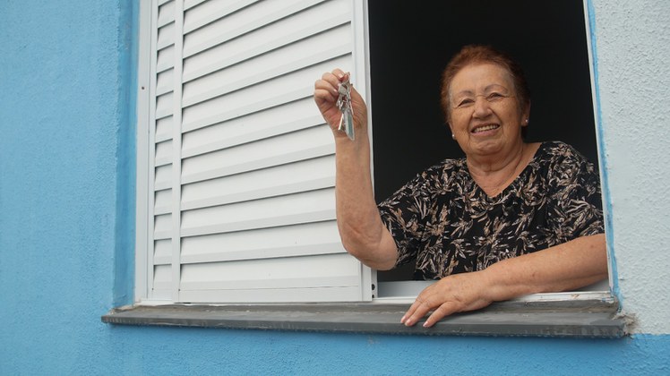 Na imagem mulher idosa na janela de sua casa 